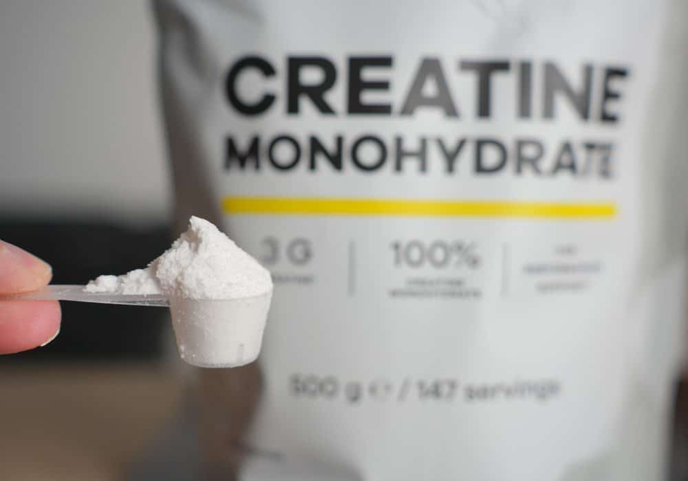 Heaped scoop of creatine monohydrate powder in front of a creatine bag
